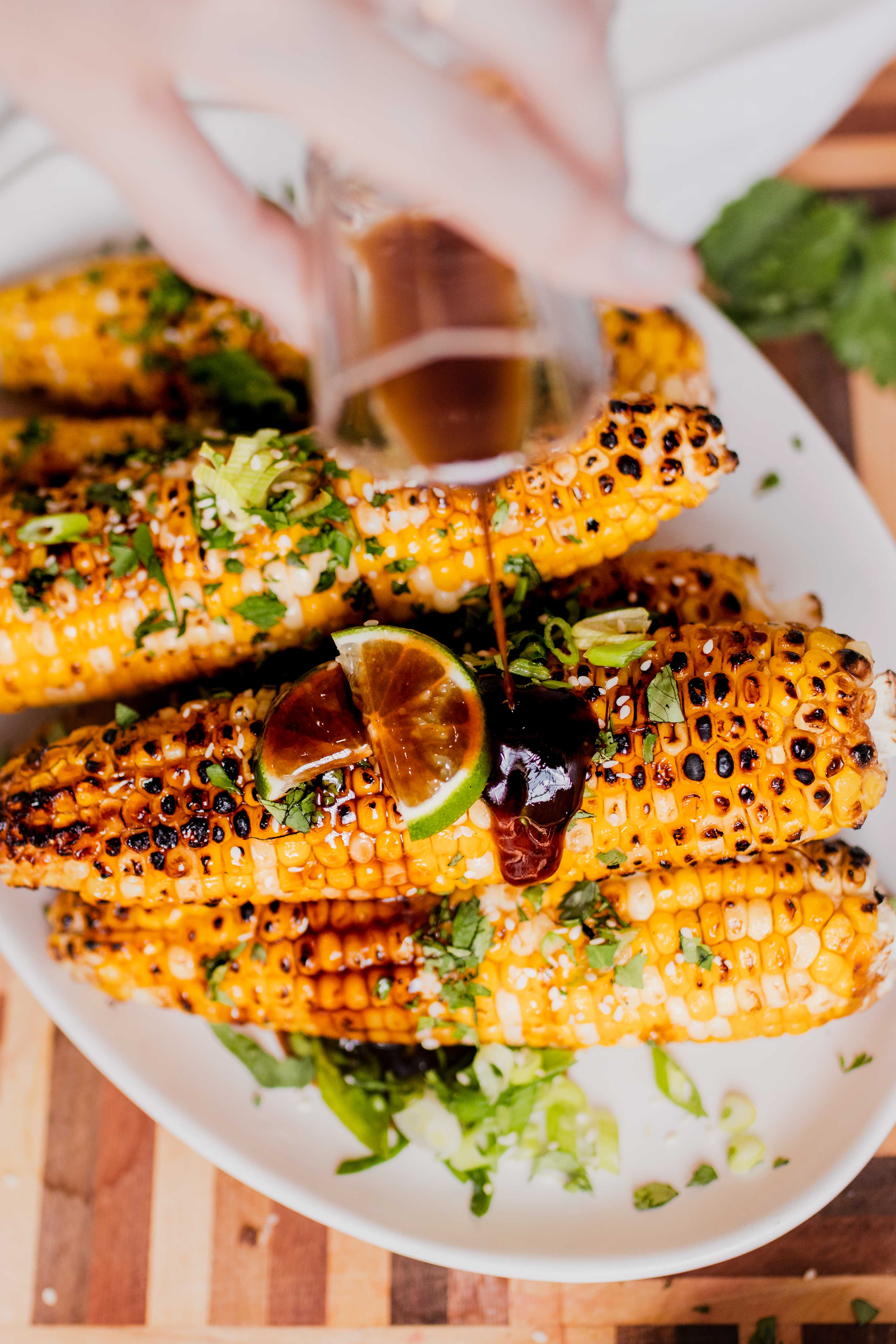 sesame glazed corn on the cob with glaze being poured over top