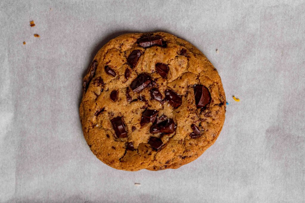 One large vegan chocolate chunk cookie on a piece of parchment paper.
