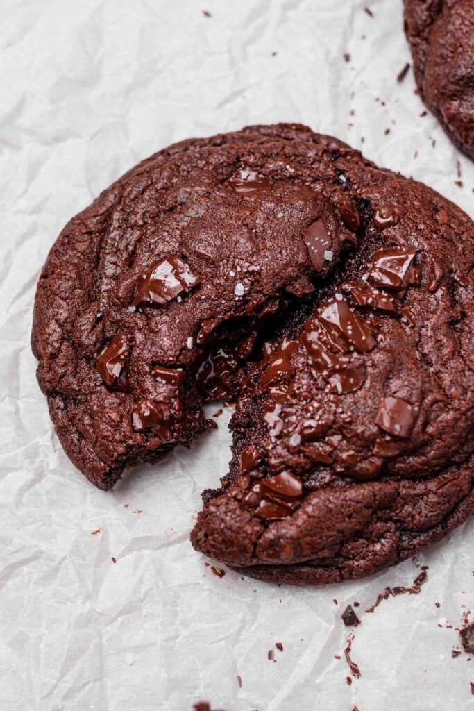 Close up shot of a vegan brownie cookie split down the middle with gooey chocolate oozing out the centre. 